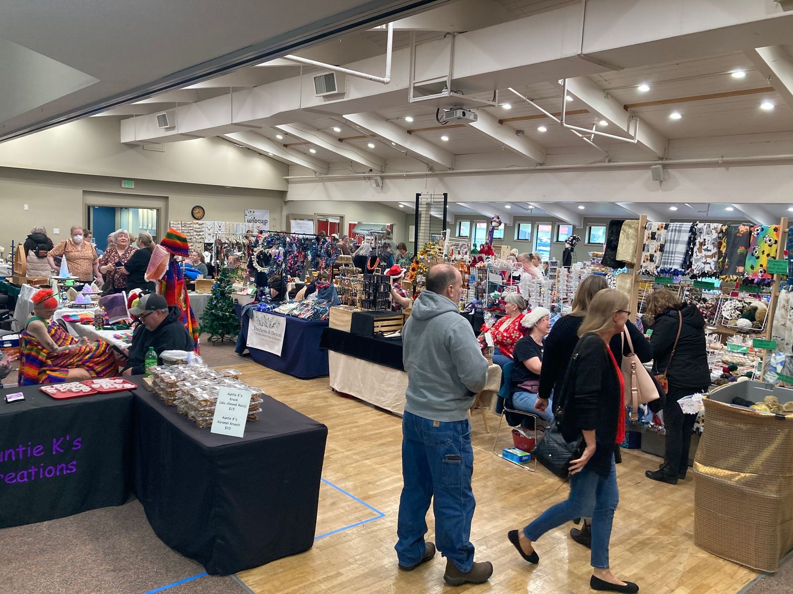 Shoppers browsing rows of vendor tables with baked goods, jewelry, and knit items in Grace's hall